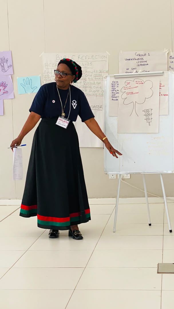 A facilitator speaks beside a flip chart headed Bible Reflection, Hebrews 10:24-25.