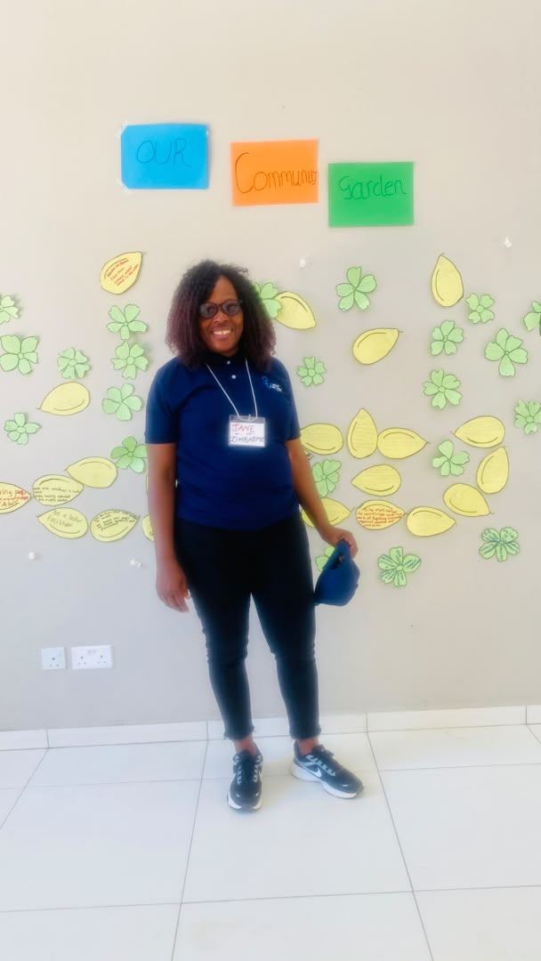 A participant stands in front of a wall headed Our Community Garden, hung with paper leaves and flowers.