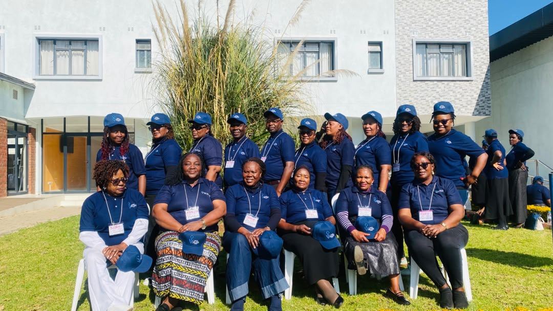 Participants in navy Speak One Voice polo shirts and caps seated and standing on a lawn.