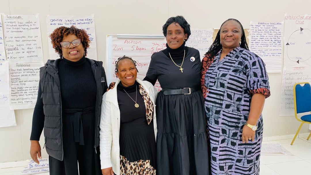 Four participants stand together in front of flip charts recording the group’s action plan.