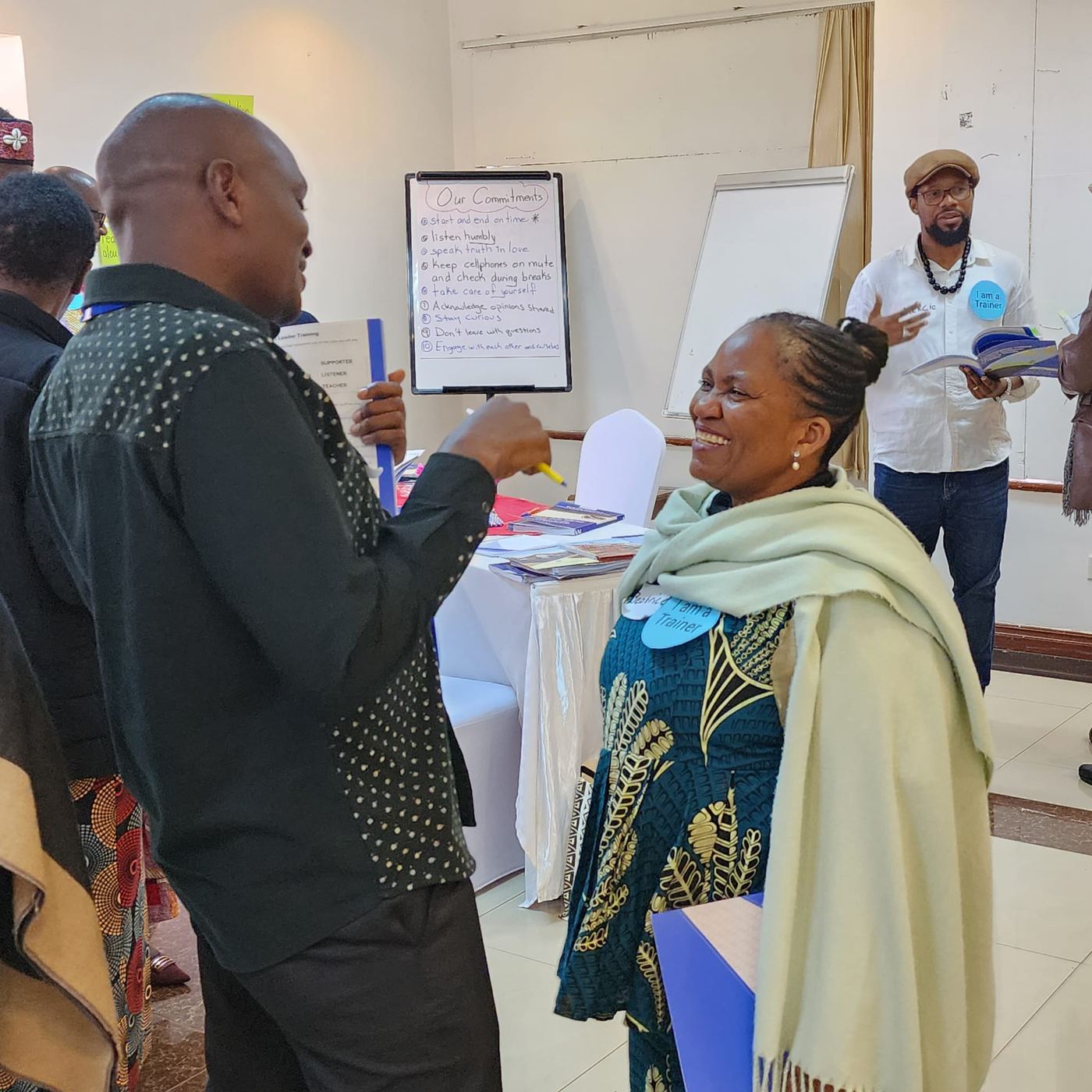 Participants talk in a workshop room, one holding a marker beside a flip chart of written points.